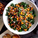 Kale salad with sweet potatoes in a white bowl, a linen napkin and a gray napkin.