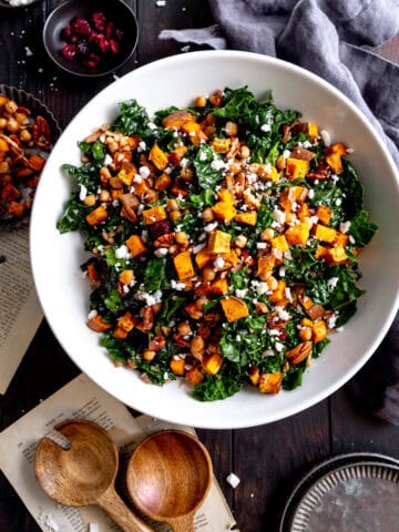 Kale salad with sweet potatoes in a white bowl, a linen napkin and a gray napkin.
