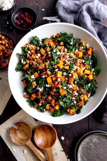 Kale salad with sweet potatoes in a white bowl, a linen napkin and a gray napkin.