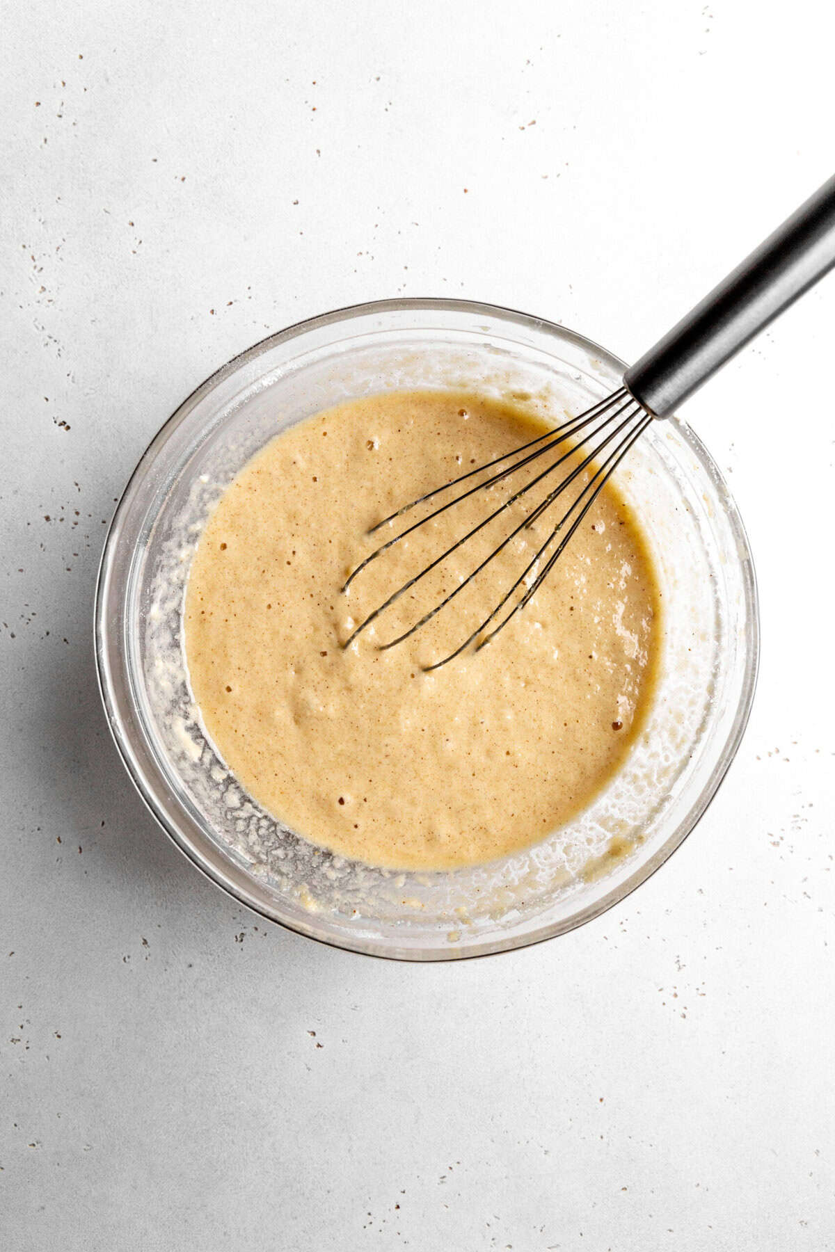 Apple cider cake batter in a glass bowl with a wire whisk.