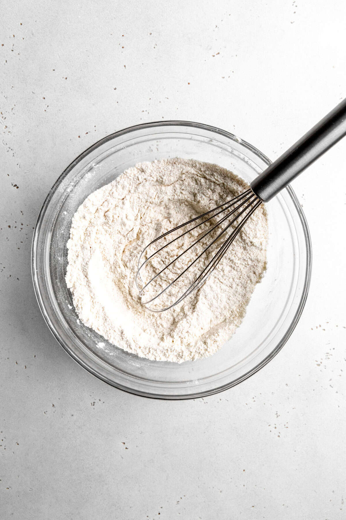 Glass bowl of flour and a wire whisk.