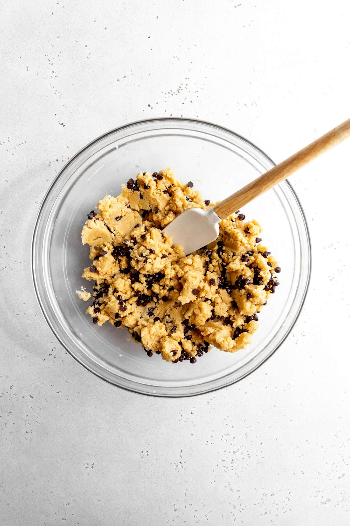 Glass bowl of chocolate chip cookie dough and a rubber spatula.