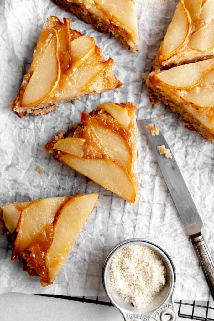 Slices of pear upside down cake on a wire cooling rack with a knife.