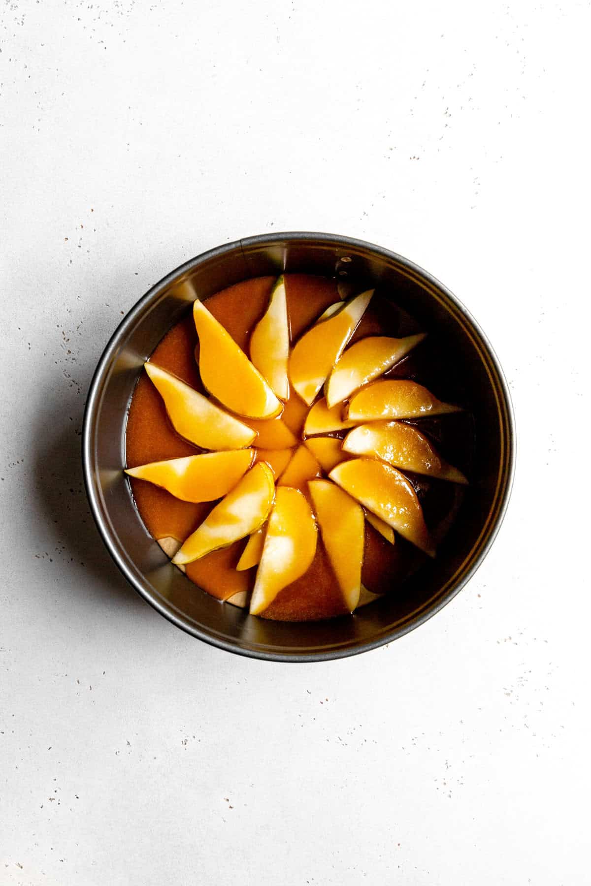 Pear slices in the bottom of a round cake pan covered in caramel sauce.