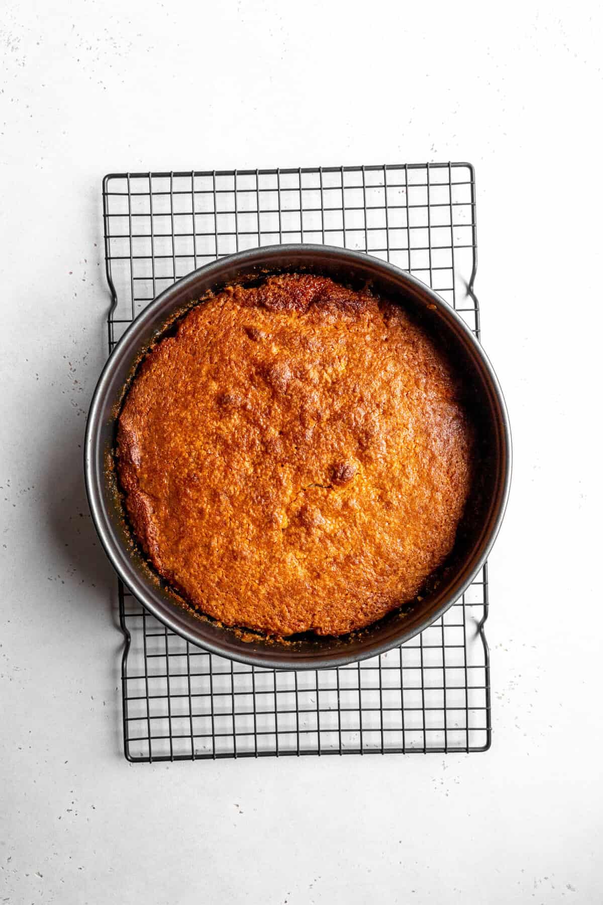 Baked pear upside down cake in a round cake pan on a wire cooling rack.