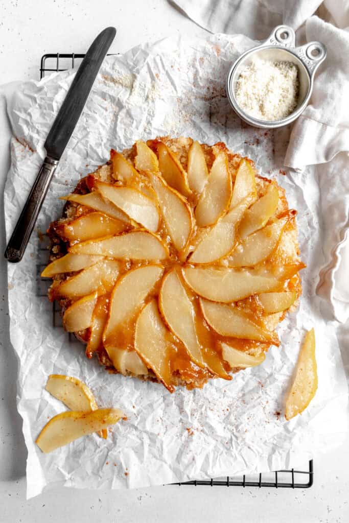 Pear upside down cake, a cup of almond flour, a napkin and a knife.