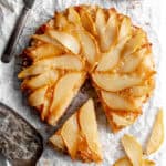 Pear upside down cake on a wire cooling rack with a cake spatula.