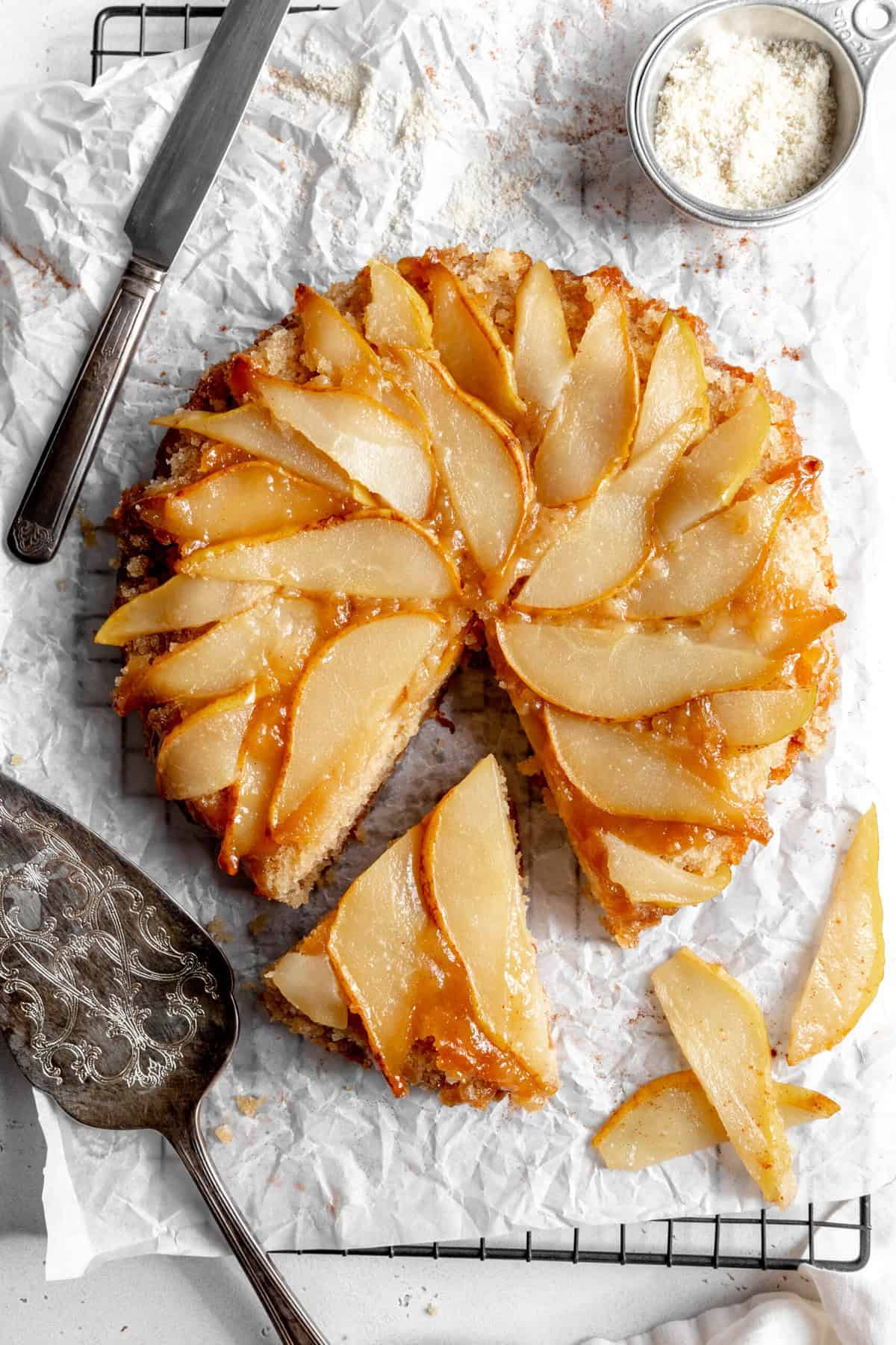 Pear upside down cake on a wire cooling rack with a cake spatula.