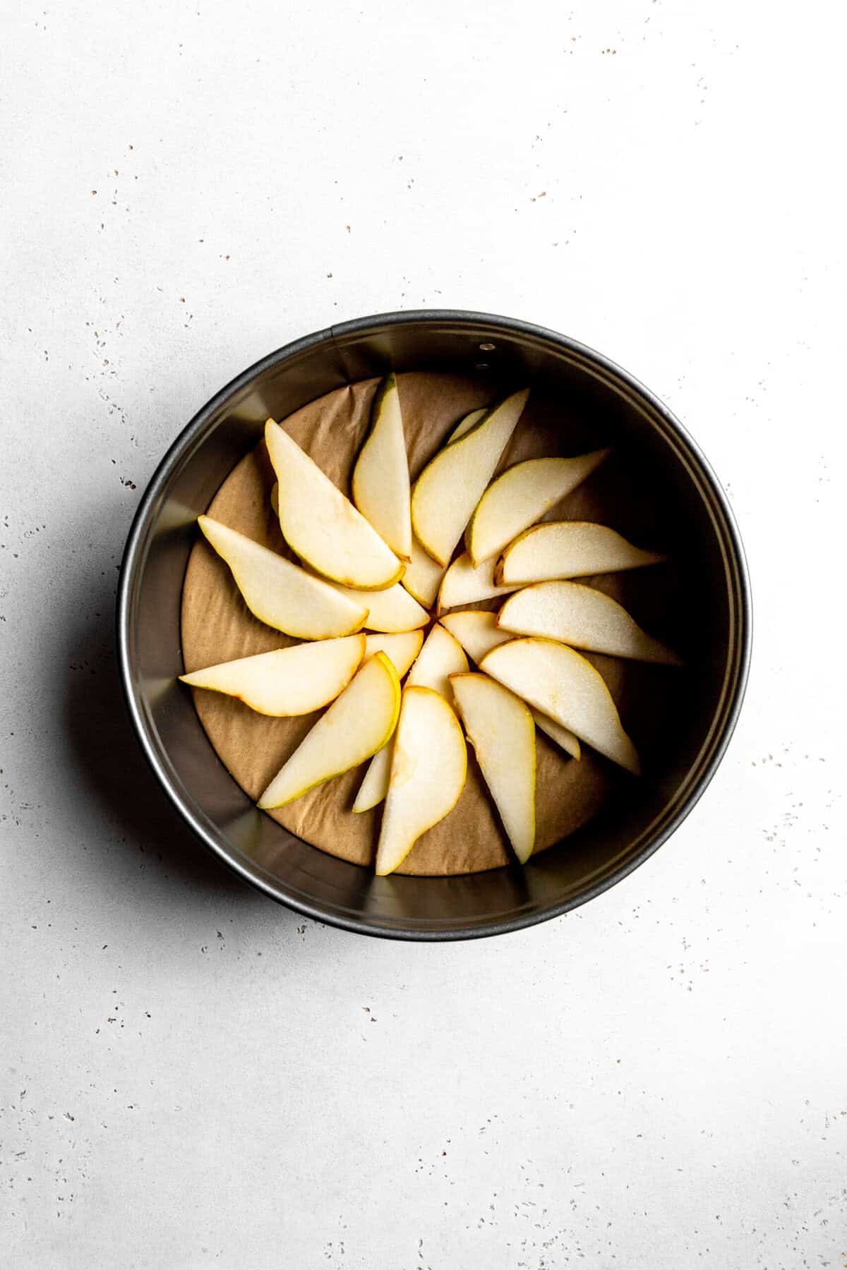 Pear slices in the bottom of a round cake pan.