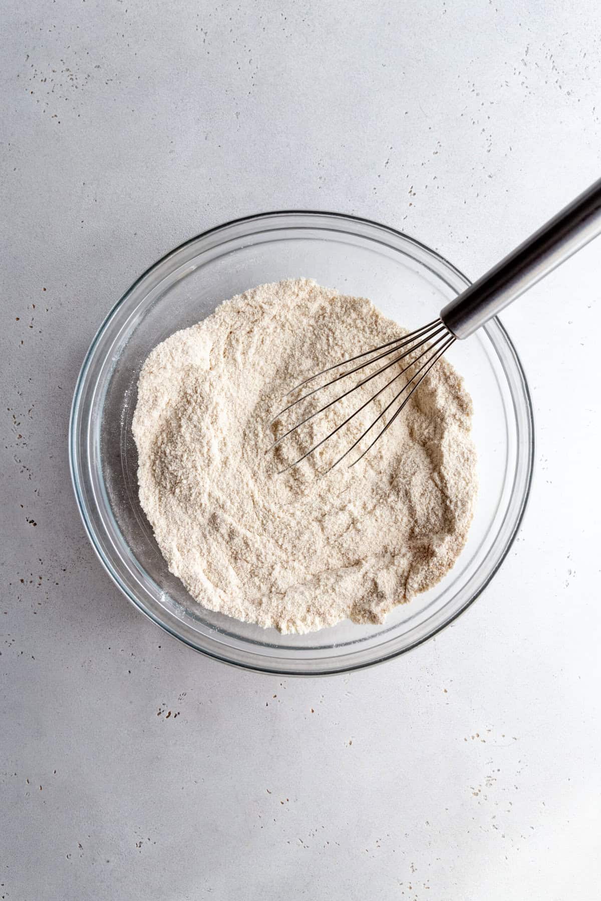 Glass bowl of flour with a whisk.