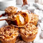 Pumpkin muffin with cream cheese filling with a bite taken out of it on a wire rack.
