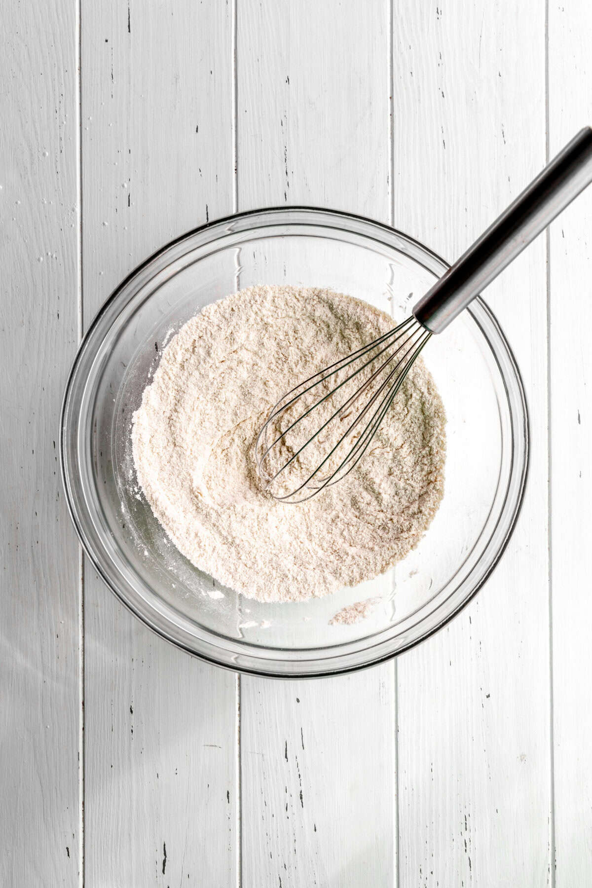 Glass bowl of flour with a wire whisk.