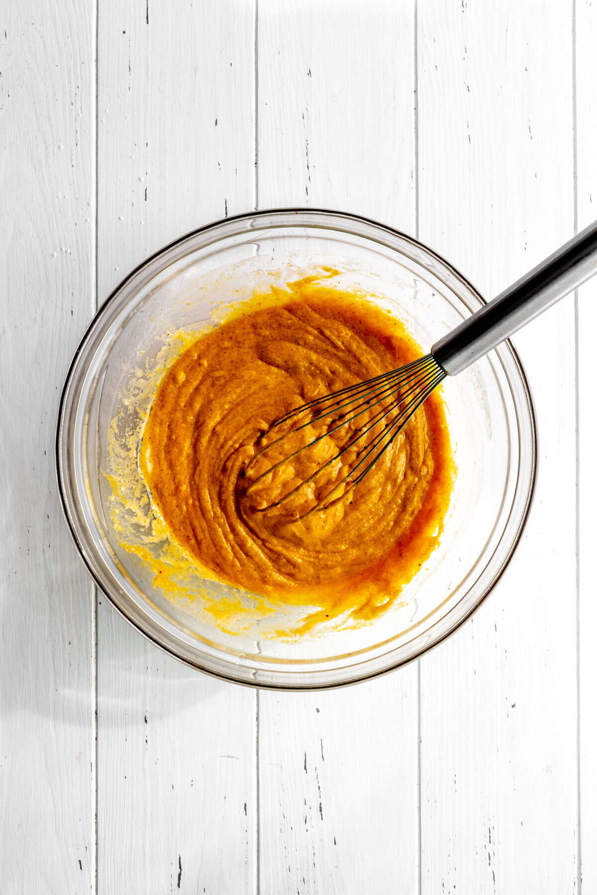 Glass bowl of pumpkin muffin batter and a wire whisk.