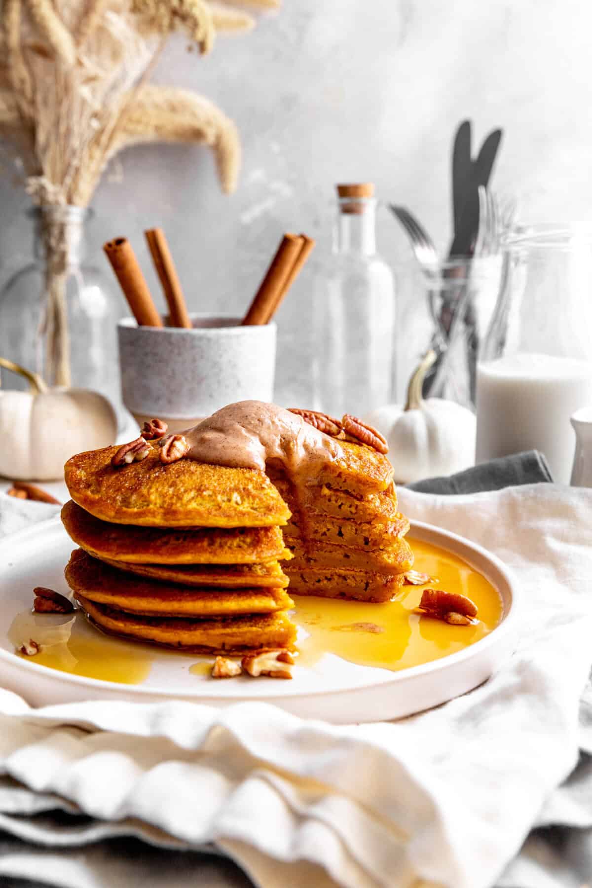 Stack of pumpkin pancakes with a triangle cut out in front of a cup of cinnamon sticks.