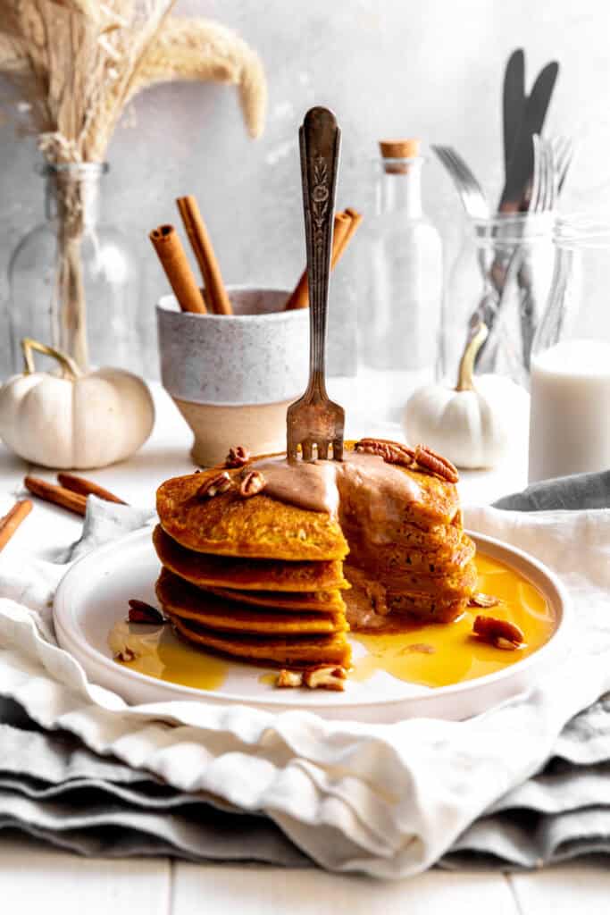 Fork sticking into a stack of pumpkin pancakes.