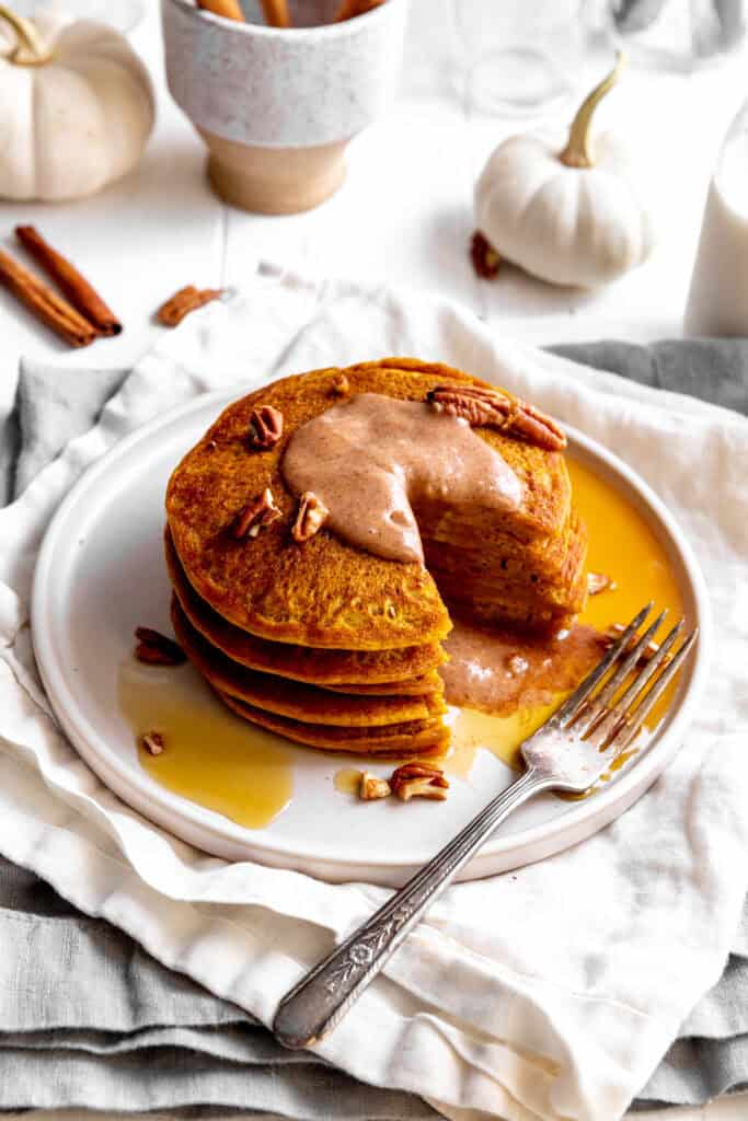 Stack of pumpkin pancakes with a triangle cut out on a plate with a fork.