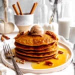 Stack of pumpkin pancakes on a plate with a fork, topped with cinnamon butter.