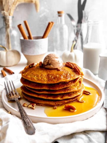 Stack of pumpkin pancakes on a plate with a fork, topped with cinnamon butter.