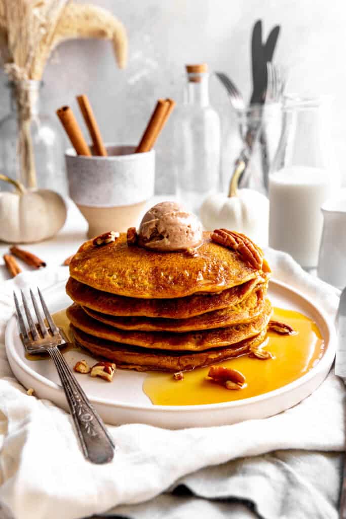 Stack of pumpkin pancakes on a plate with a fork, topped with cinnamon butter.