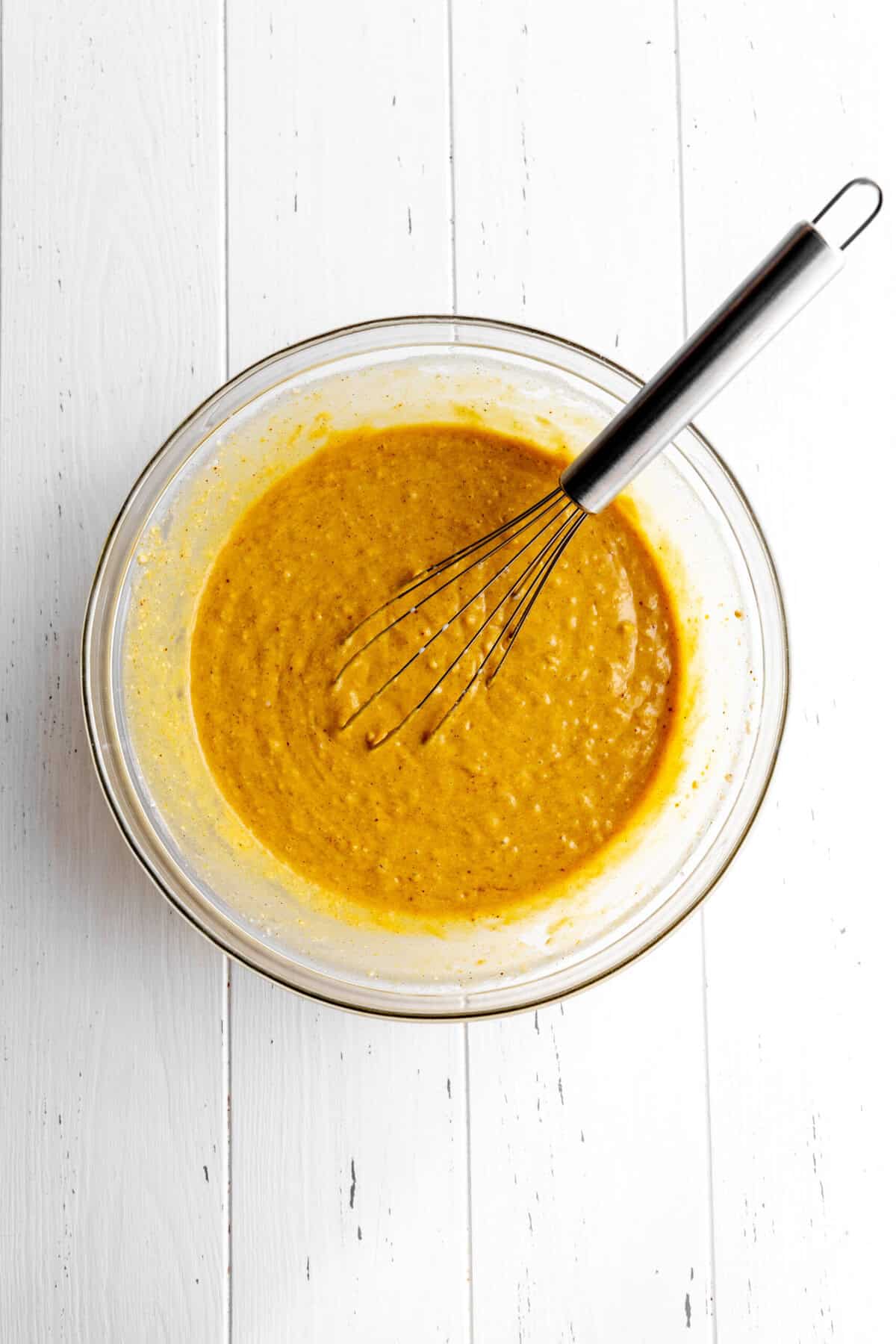 Pumpkin pancake batter in a glass bowl with a wire whisk.