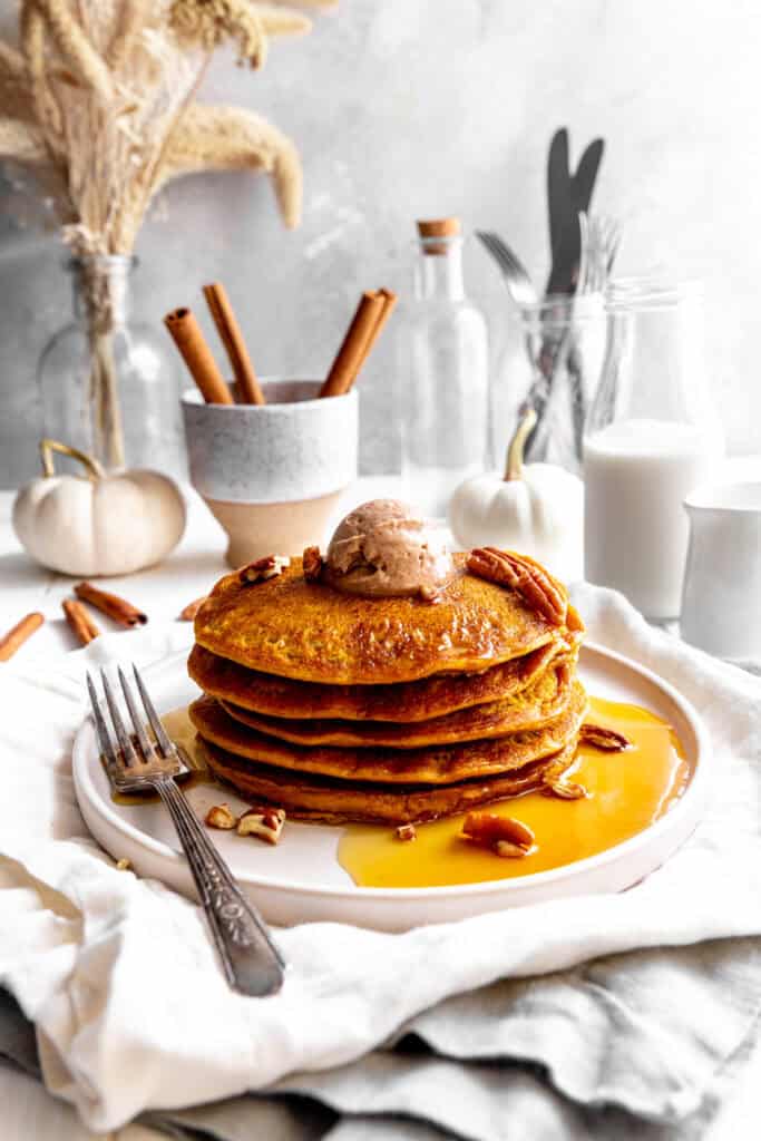 Stack of pumpkin pancakes topped with cinnamon butter and pecans on a plate with a fork.