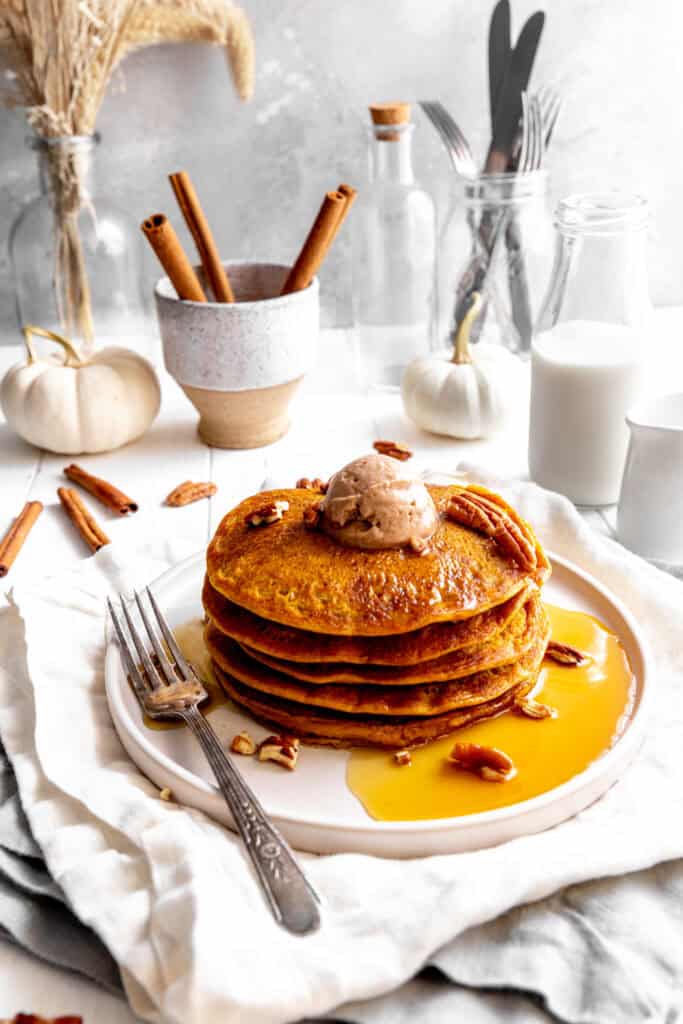 Stack of vegan pancakes on a plate, white pumpkins, a jug of milk and scattered pecans.
