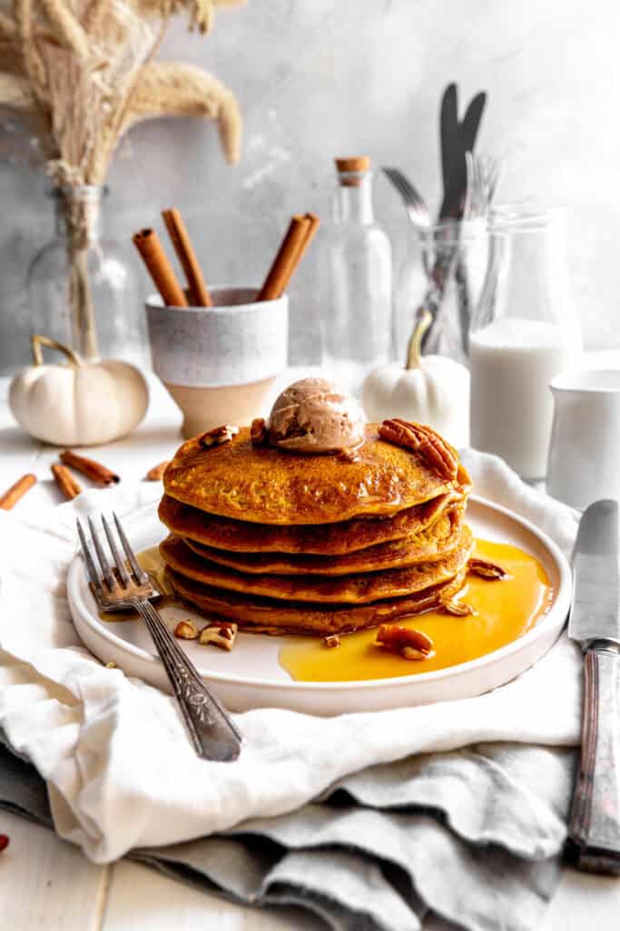 Stack of pumpkin pancakes on a plate, a jug of milk and cinnamon sticks.