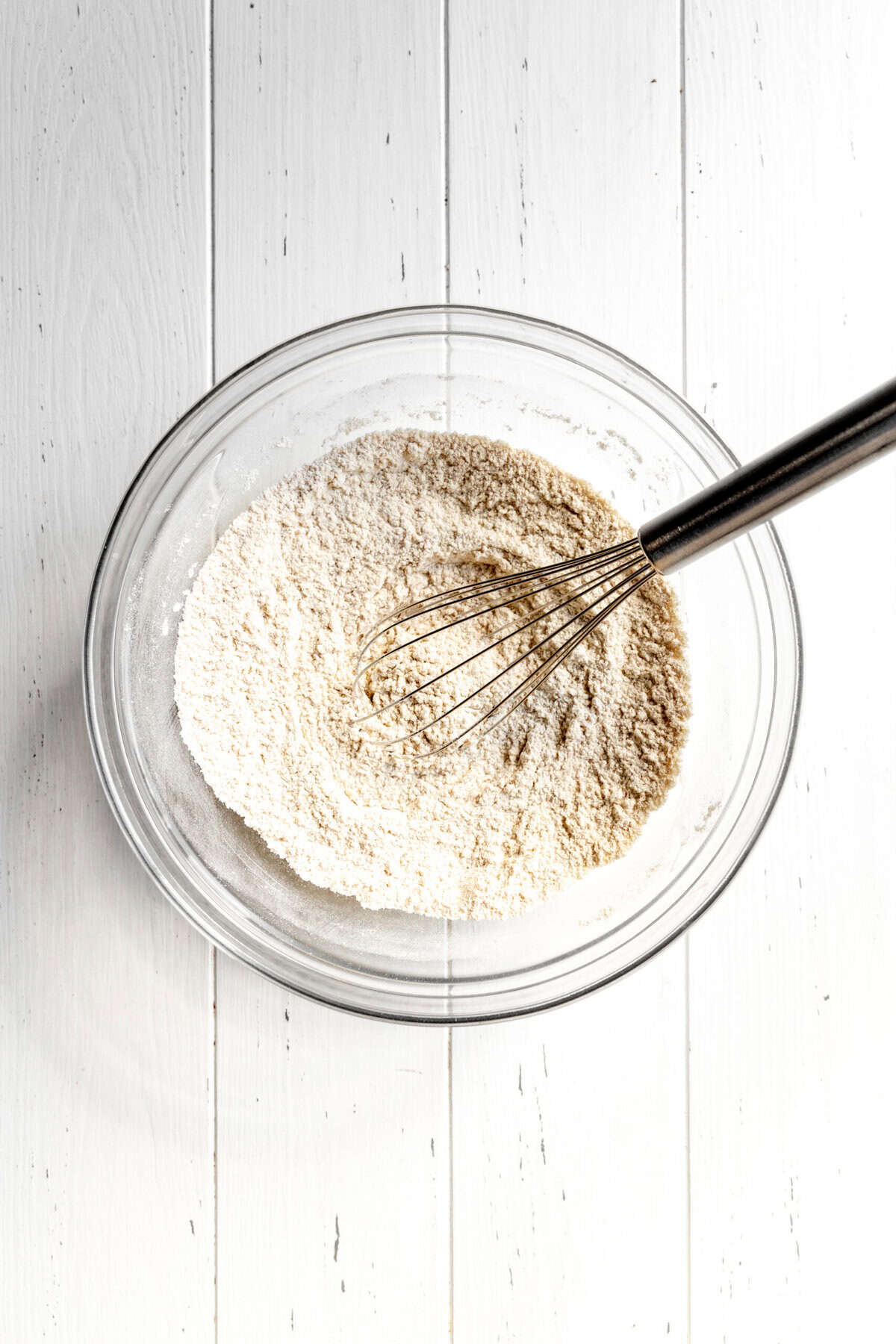 Flour and spices in a glass bowl with a wire whisk.