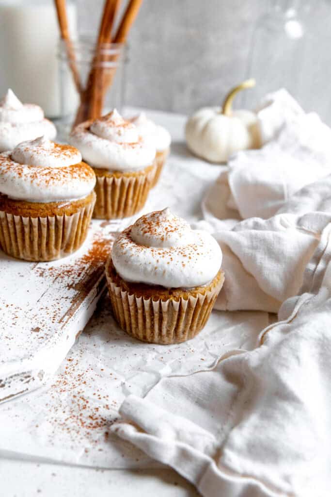 Pumpkin cupcake topped with whipped cream and a white linen napkin.
