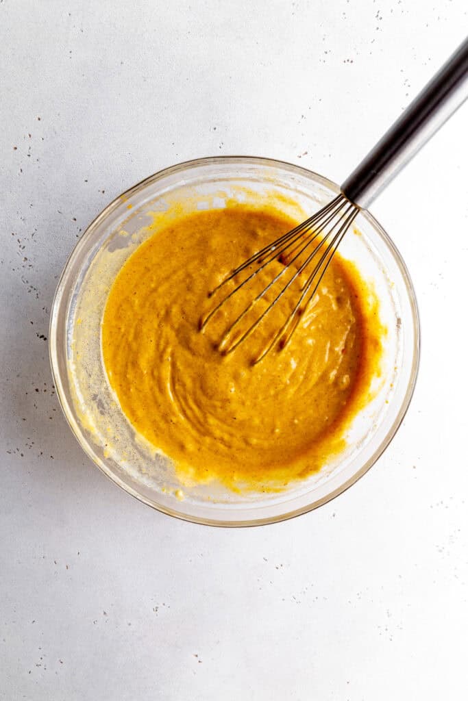 Pumpkin cake batter in a glass bowl with a wire whisk.