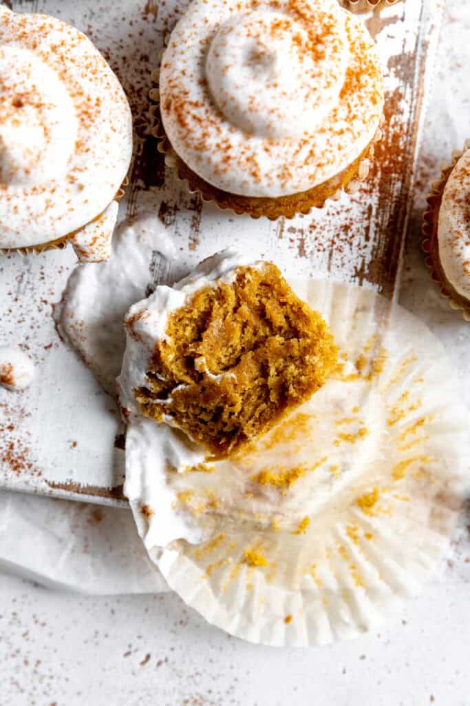 Half a pumpkin cupcake laying on a white wooden cutting board.