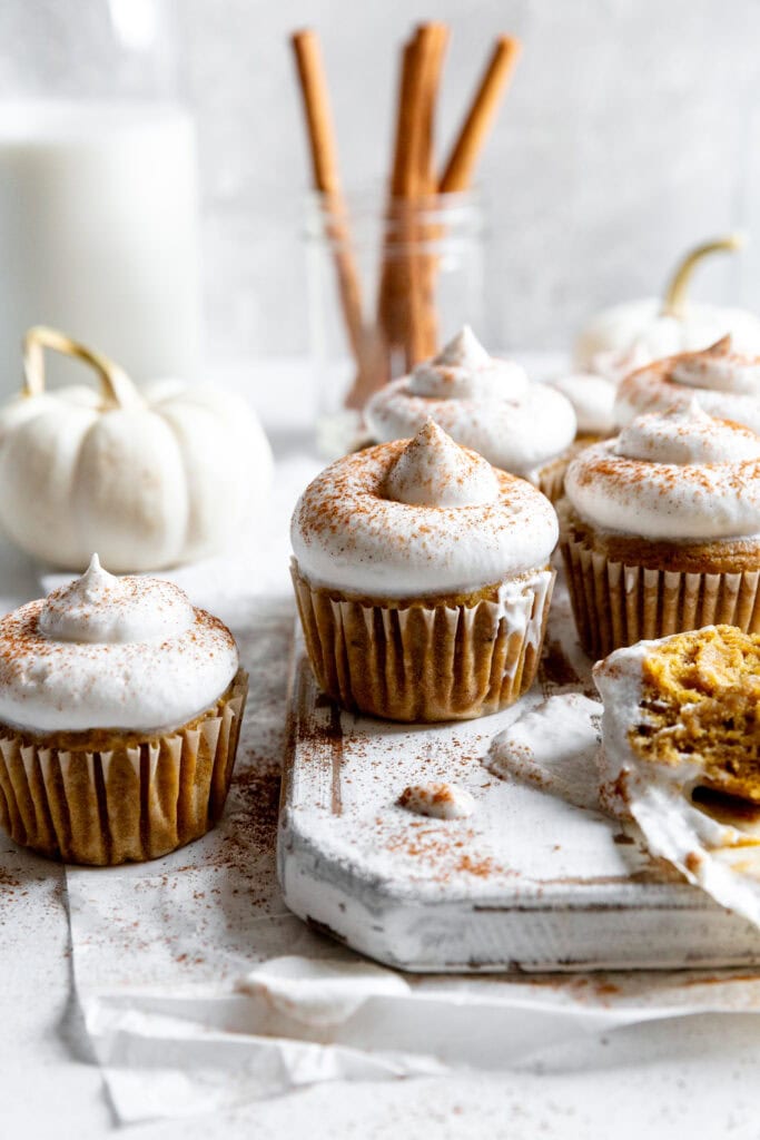 Pumpkin cupcakes topped with whipped cream on a white wooden board.