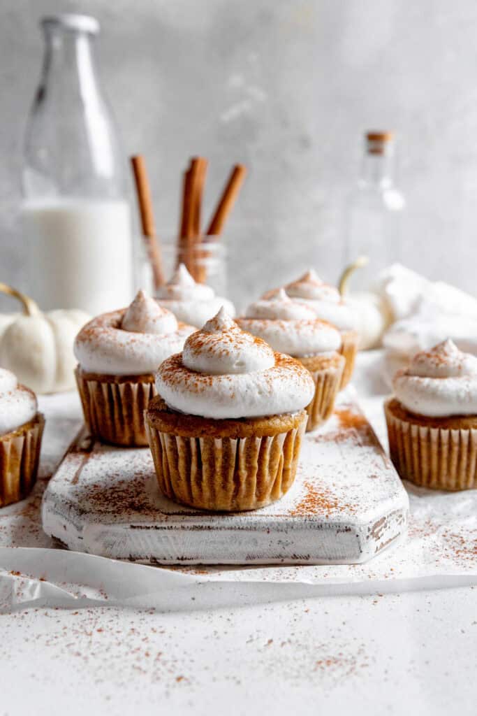 Pumpkin cupcakes with whipped cream, a jug of milk and a jar of cinnamon sticks.