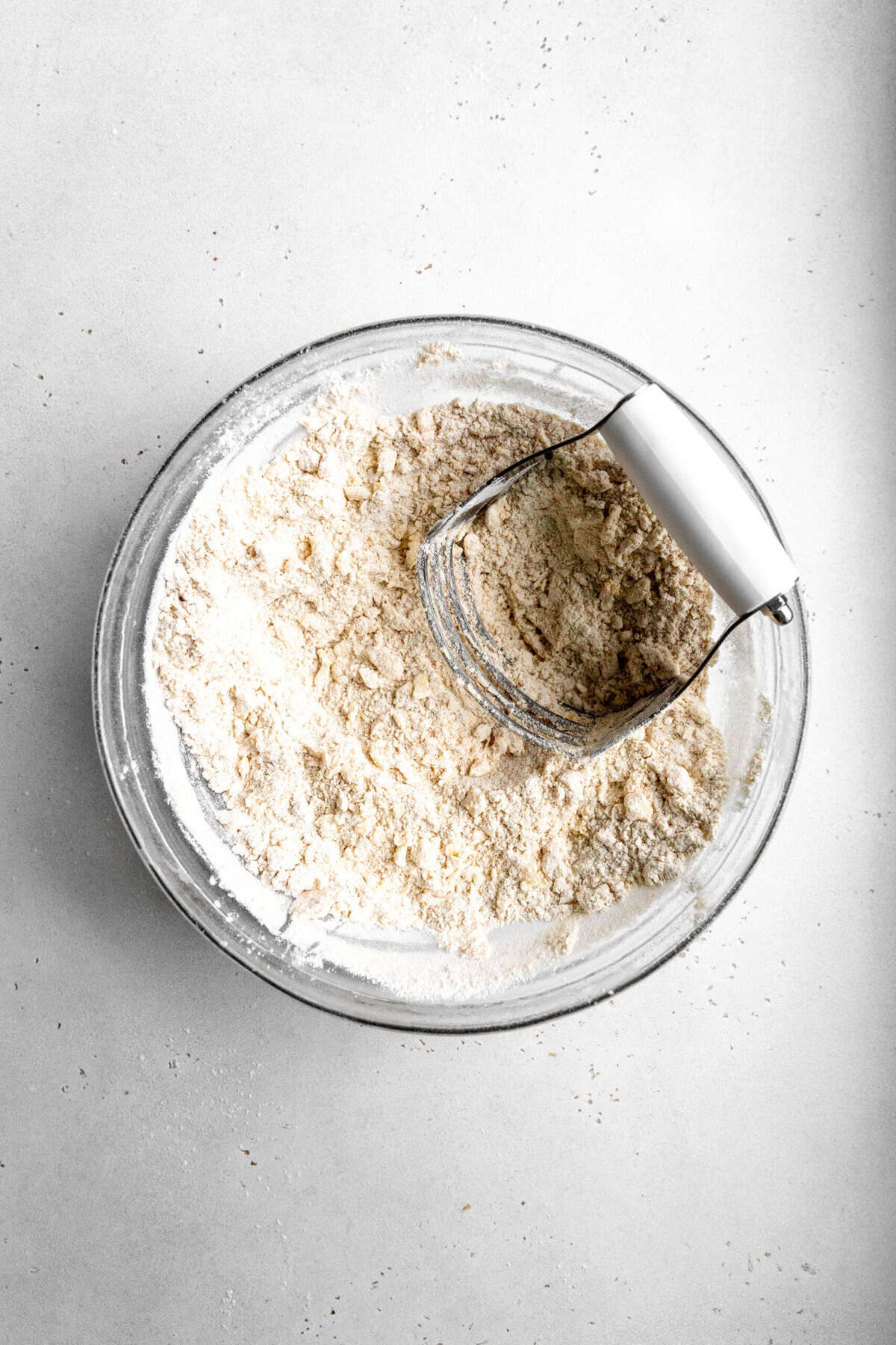 Pastry cutter cutting vegan butter into flour in a glass bowl.