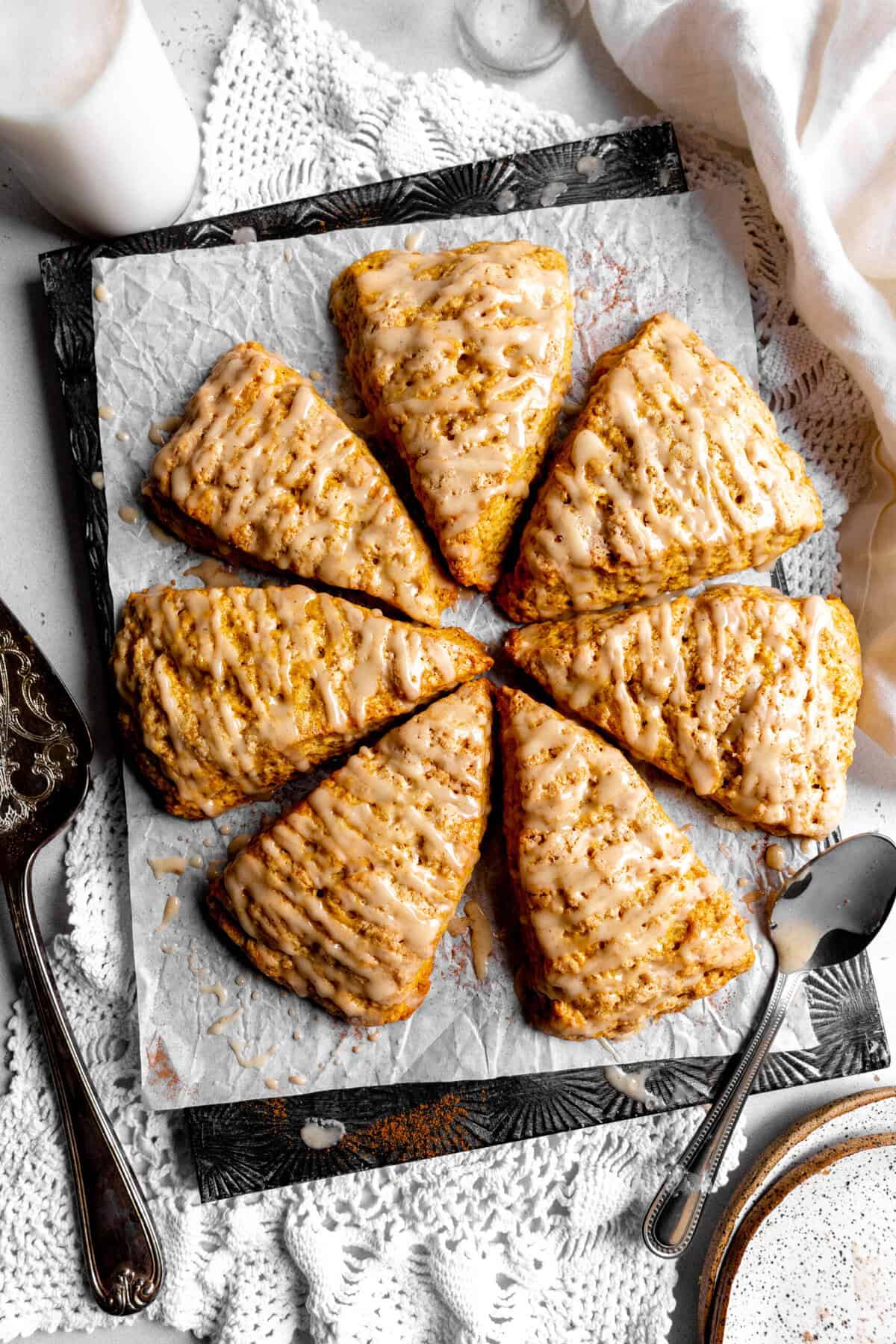 Pumpkin scones arranged in a circle on a baking sheet, a jug of milk and a napkin.