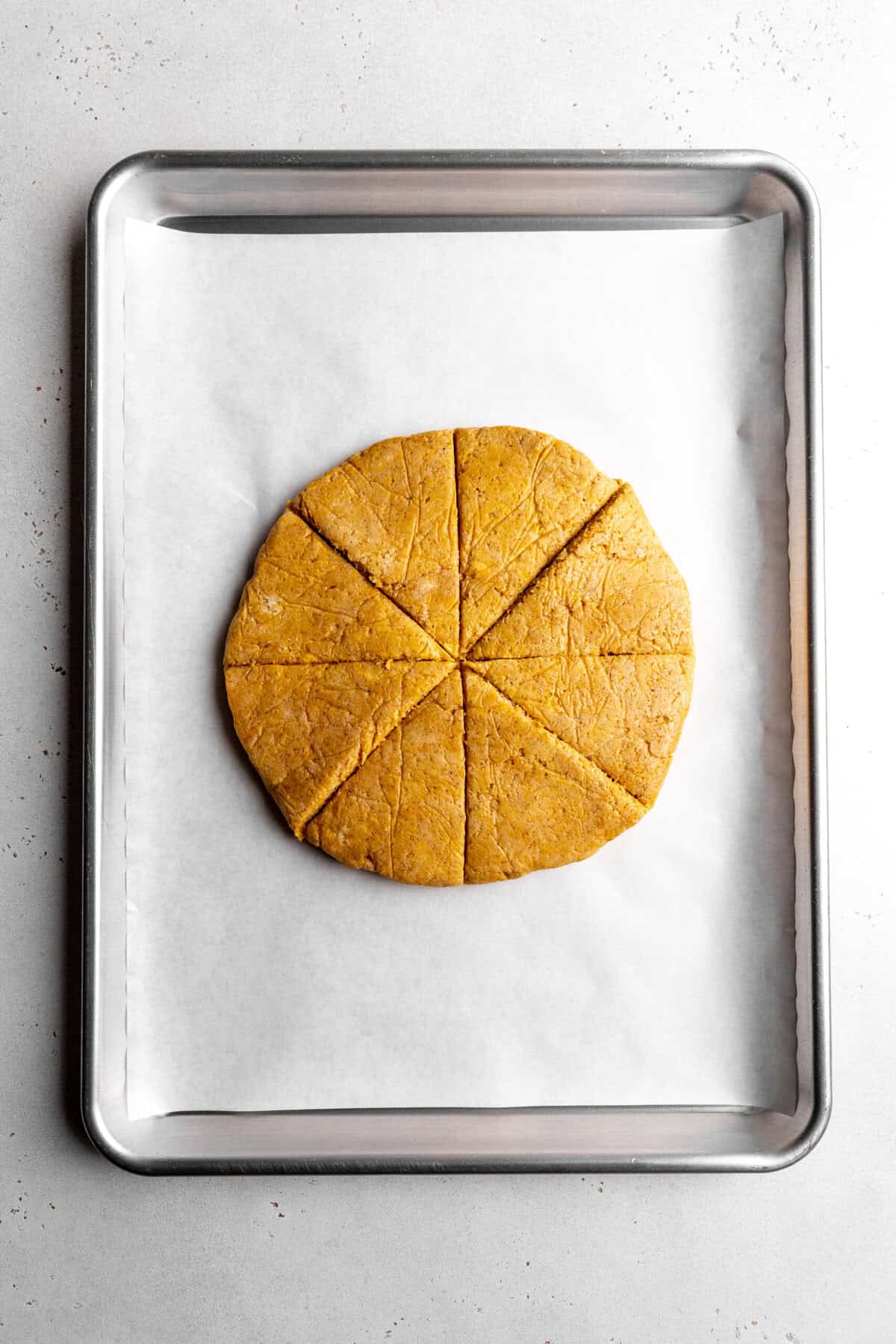 Pumpkin scone dough cut into eight slices on a baking sheet.