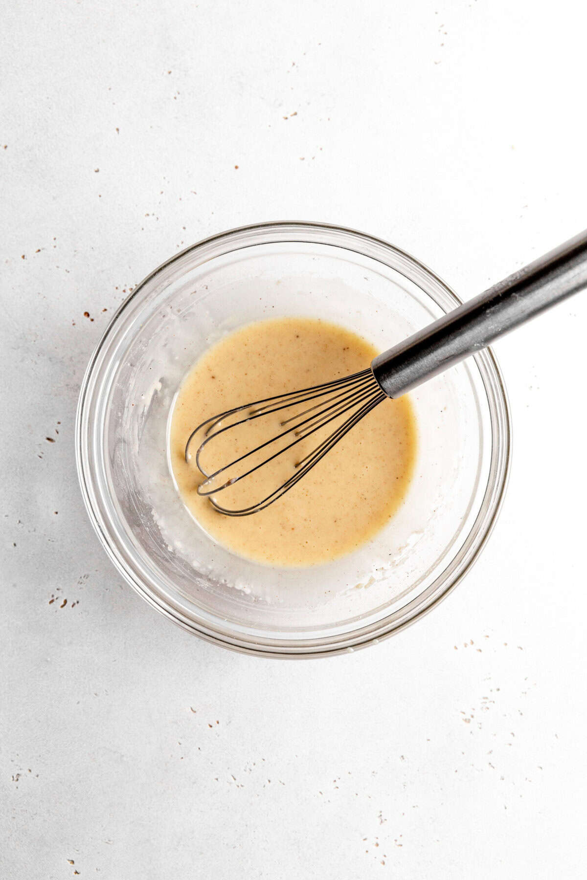 Maple glaze in a glass bowl with a wire whisk.