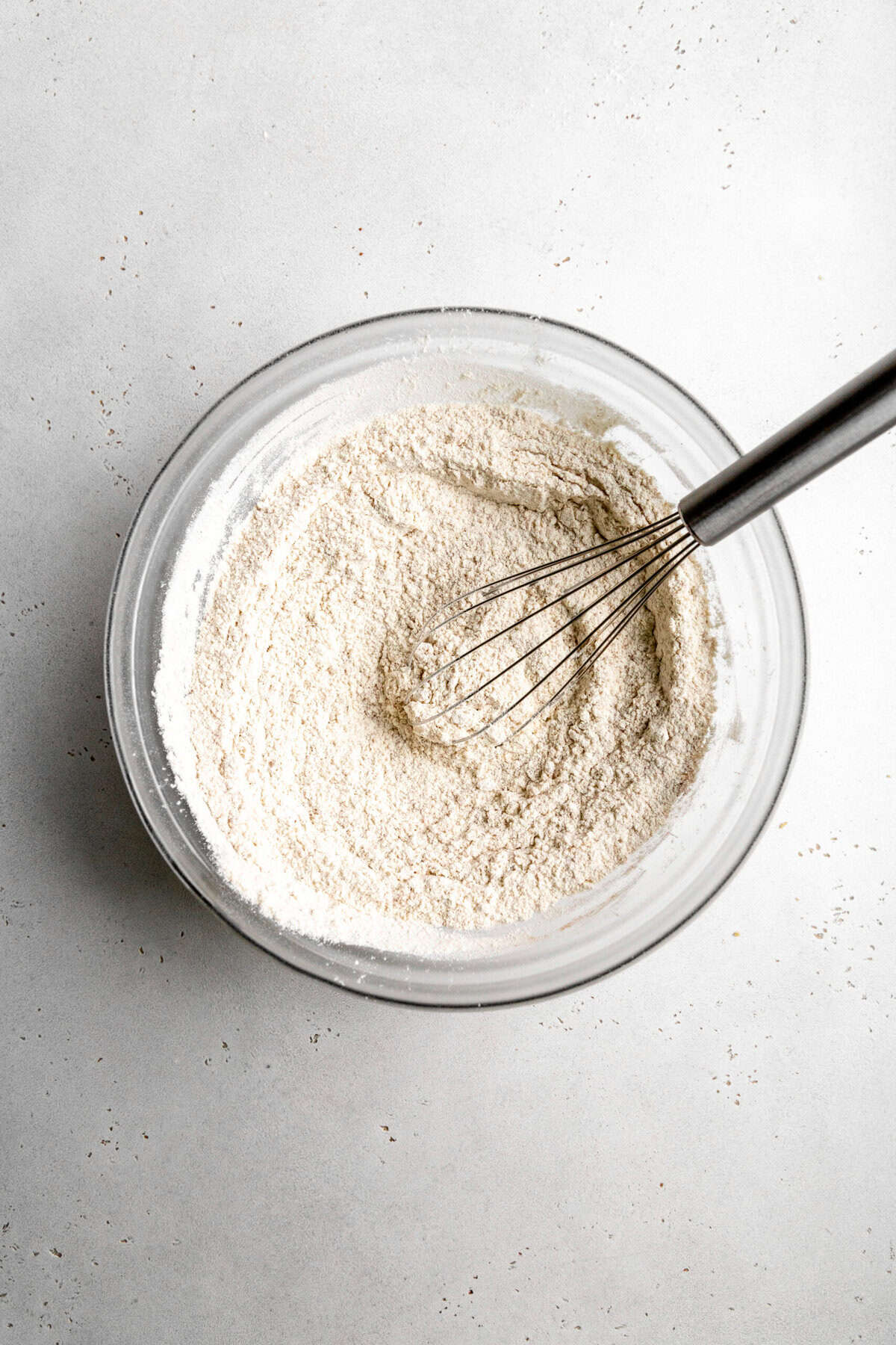 Flour and sugar in a glass bowl with a wire whisk.