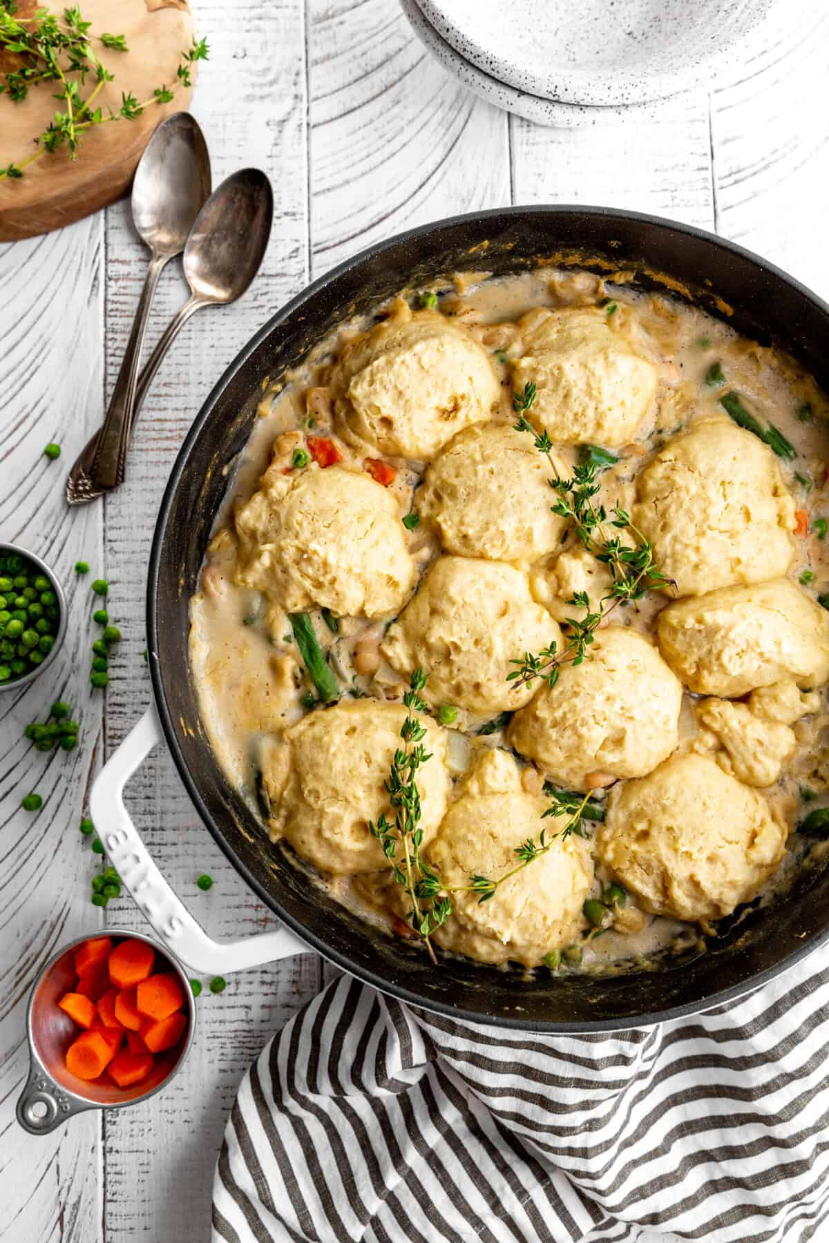 Pot of vegetable pot pie soup, two spoons, a linen napkin and a cup of chopped carrots.
