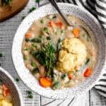 Spoon in a bowl of vegetable pot pie soup and small cups of peas and carrots.