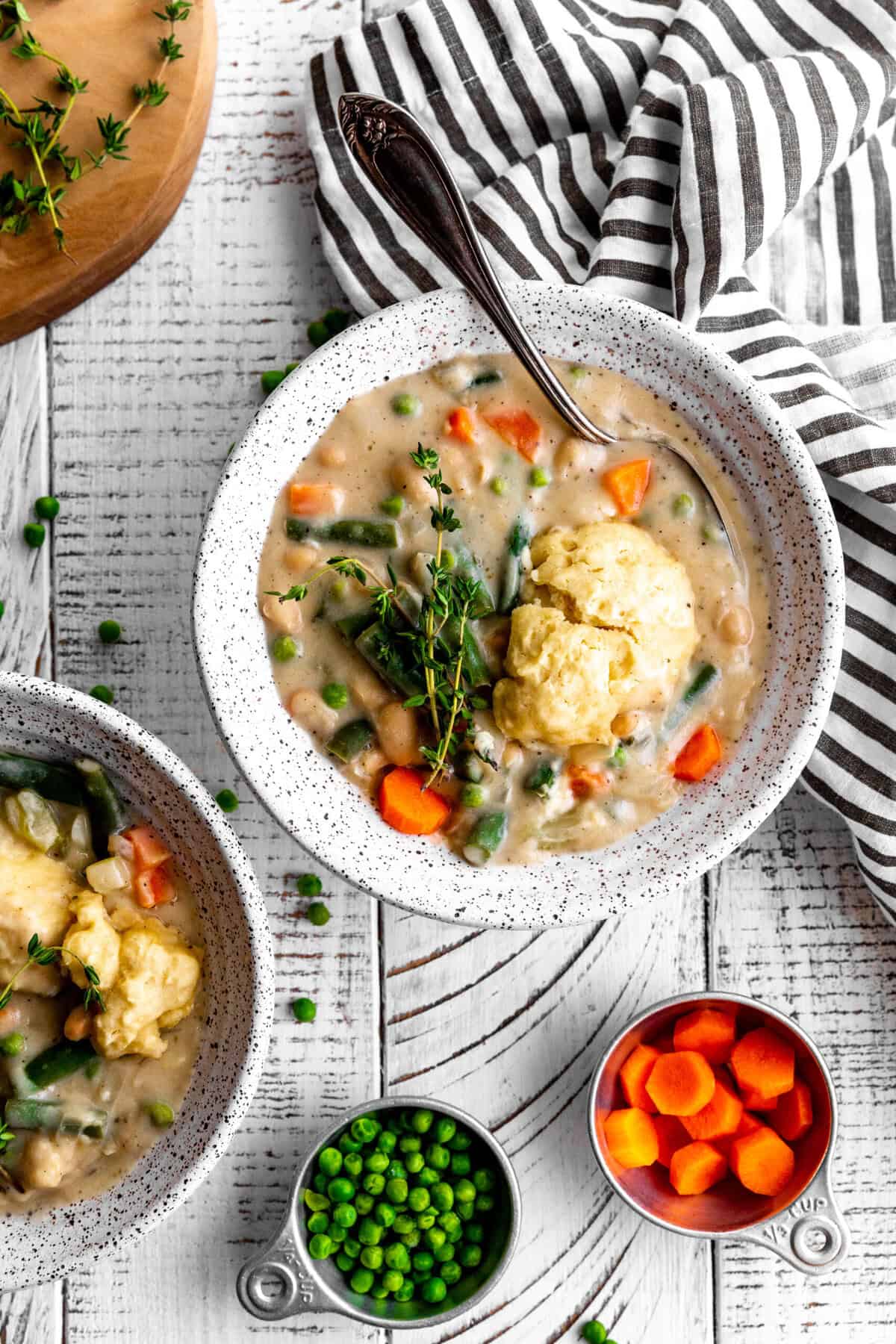 Bowls of vegetable pot pie soup on a white wooden tabletop with a napkin.