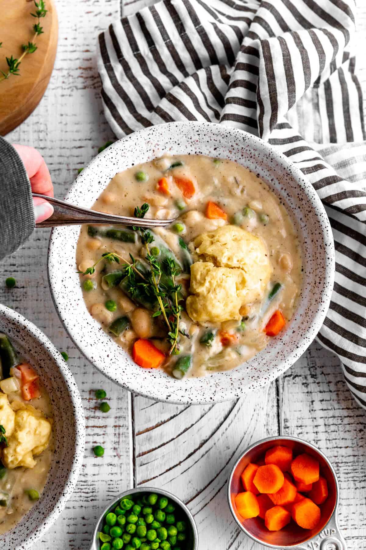 Hand holding a spoon digging into a bowl of vegetable pot pie soup.