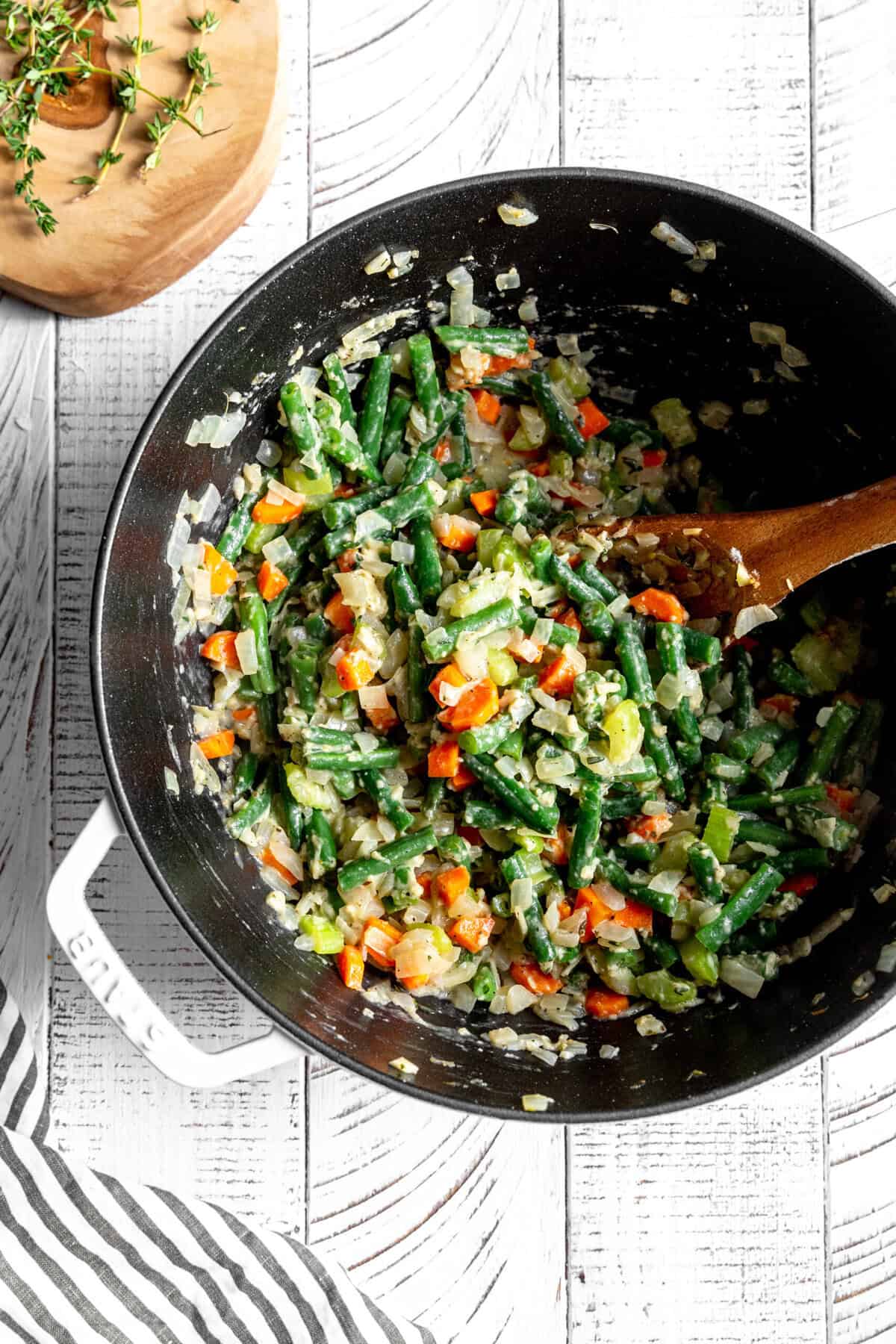 Sautéed onions, carrots, celery, green beans and flour in a pot with a wooden spoon.