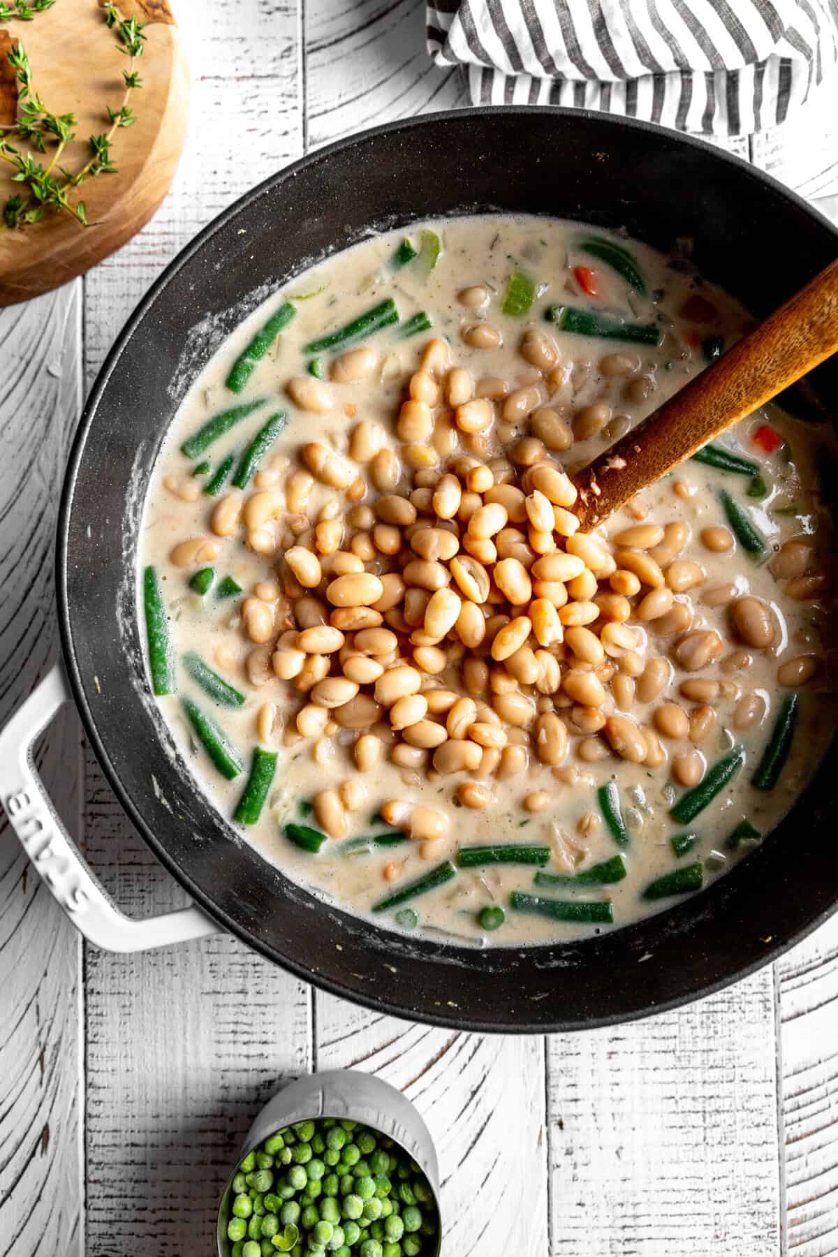 White beans poured into a pot of vegetable soup.