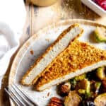 Baked tofu cutlets cut into triangles on a plate with brussels sprouts.