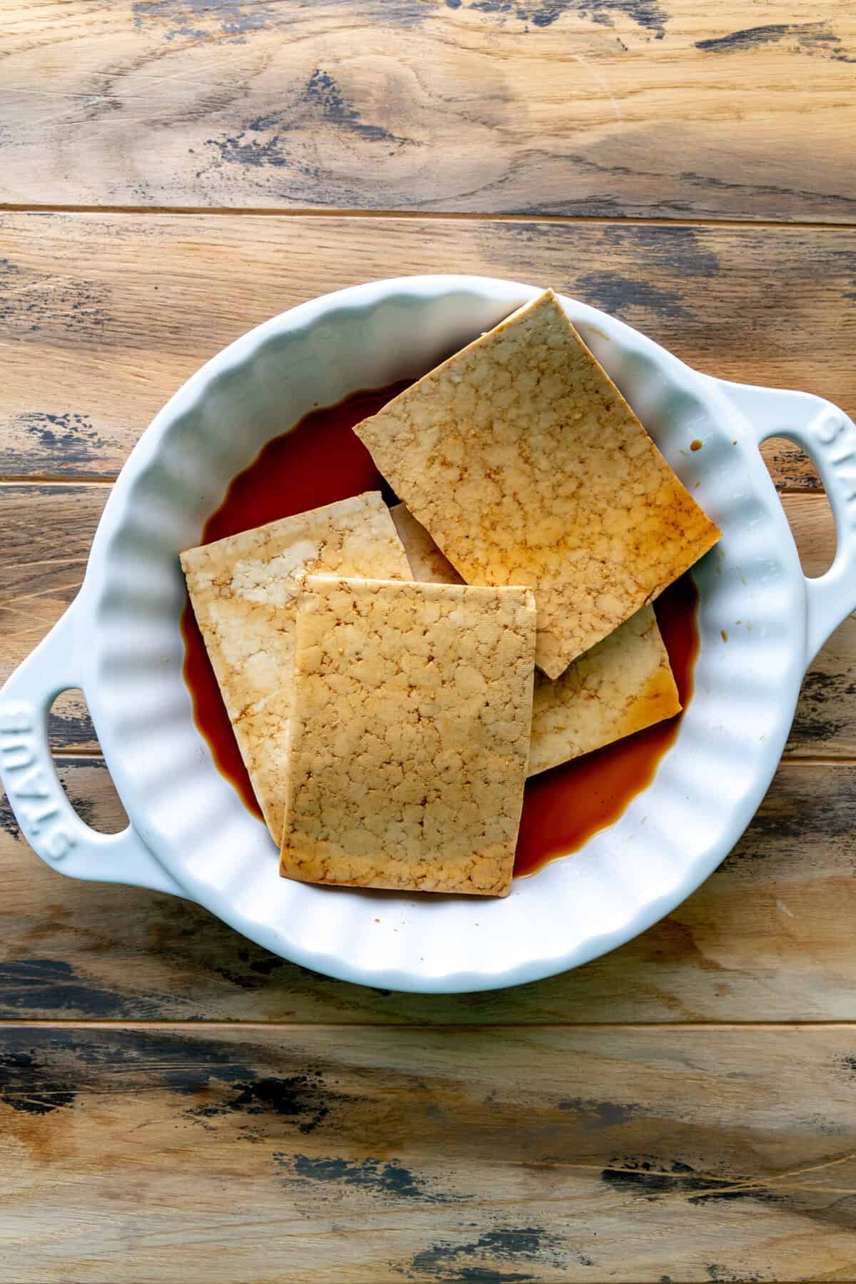 Slabs of tofu marinating in a shallow dish.