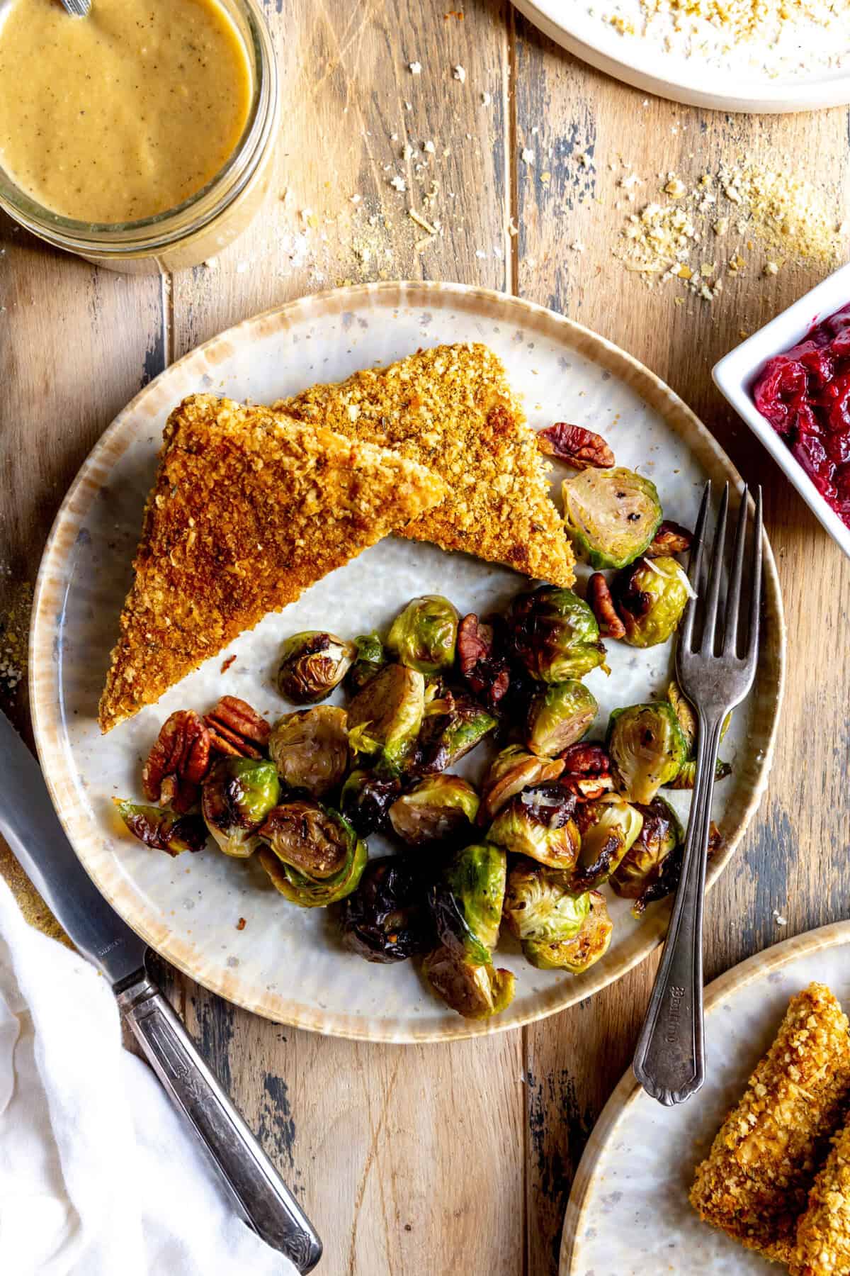 Baked tofu cutlets on a plate with brussels sprouts and a fork.