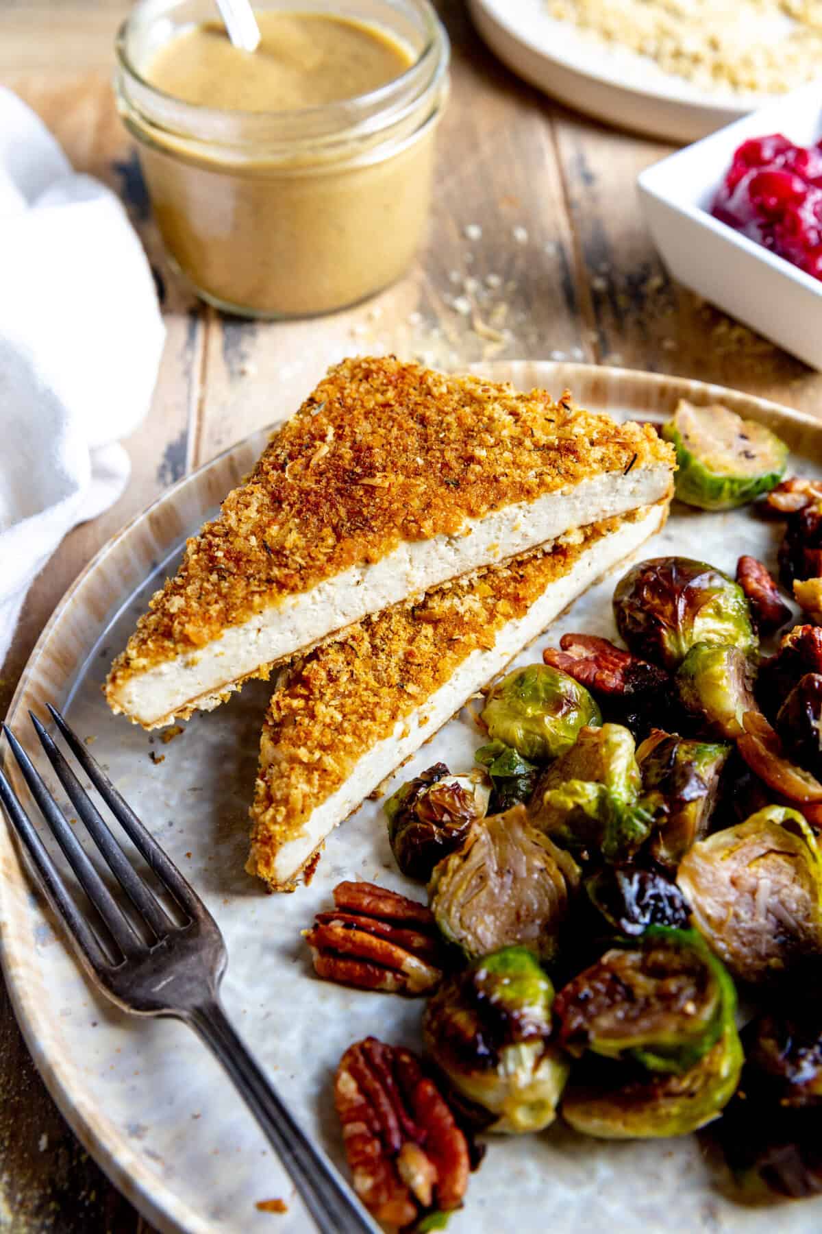 Baked tofu cutlets on a plate with brussels sprouts and a cup of gravy.