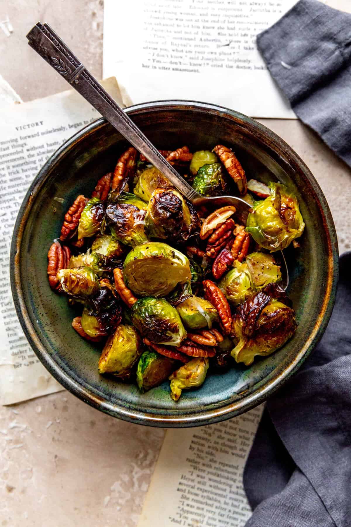 Spoon digging into a bowl of roasted brussels sprouts and pecans.