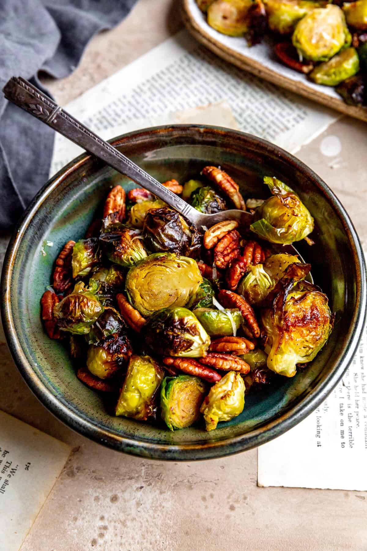 Spoon digging into a bowl of roasted brussels sprouts and pecans.
